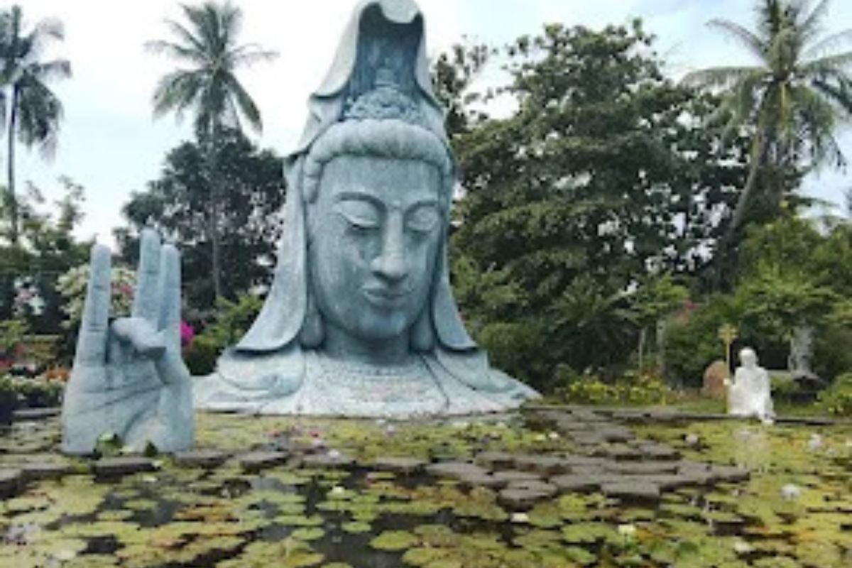 Estátua de Buda no lago de lótus do Pagode Thanh Lương em Tuy Hoa, cercada por água e elementos naturais.
