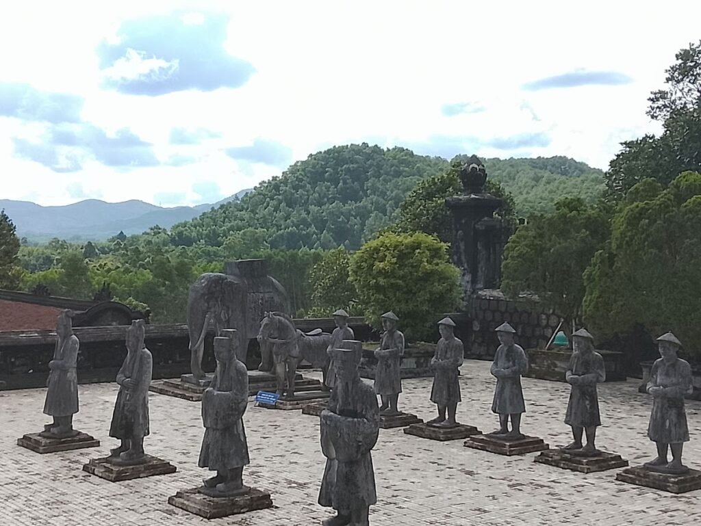 Estátuas de guardiões e animais simbólicos alinhadas em um pátio da Cidade Imperial de Huế, com colinas verdes e vegetação ao fundo, representando a herança histórica e espiritual do Vietnã centra