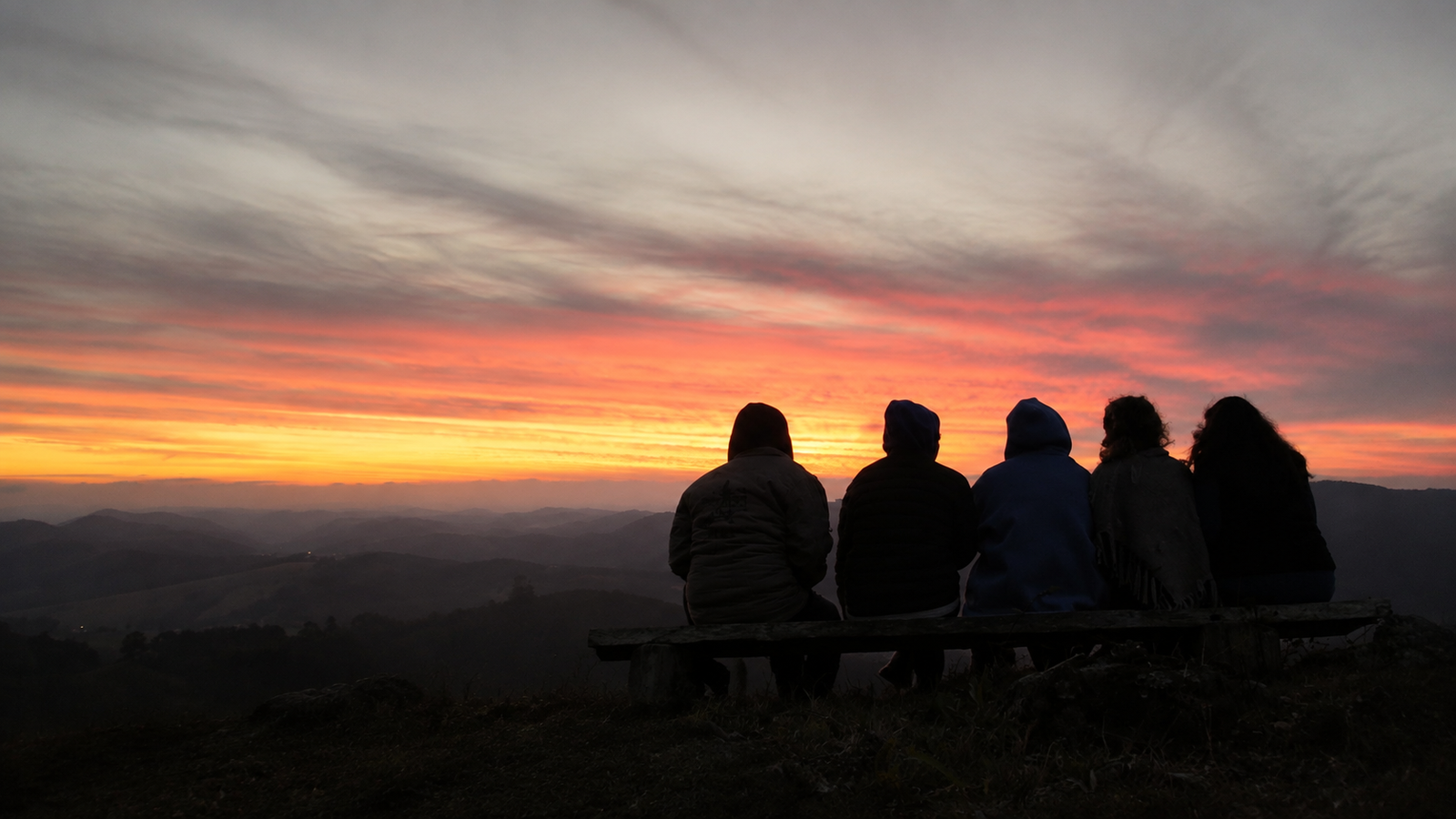 Cinco participantes do Retiro Travessias sentados de costas diante do pôr do sol nas montanhas