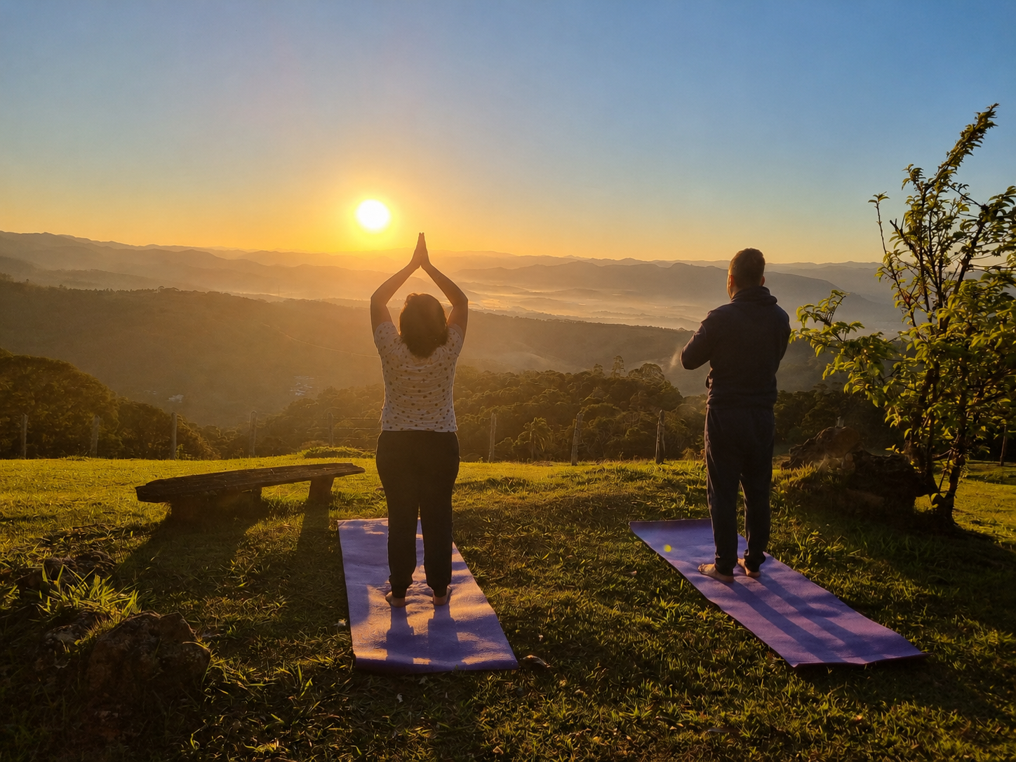 Duas pessoas praticando Yoga ao nascer do sol, diante das montanhas